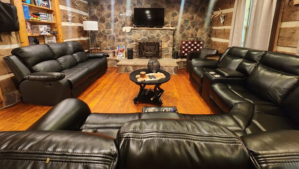 A cozy living room with leather sofas, a stone fireplace, a flat-screen TV, and a bookshelf. - Whispering Pine's Cabin! NO CHECK-OUT LIST (Patriot)