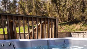 A hot tub with a wooden deck and stone wall in the background. - Whispering Pine's Cabin! NO CHECK-OUT LIST (Patriot)