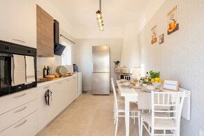 A modern kitchen with a refrigerator, oven, and a dining area with a table and chairs. - Stardust - A Haven of Elegance (Ostuni)