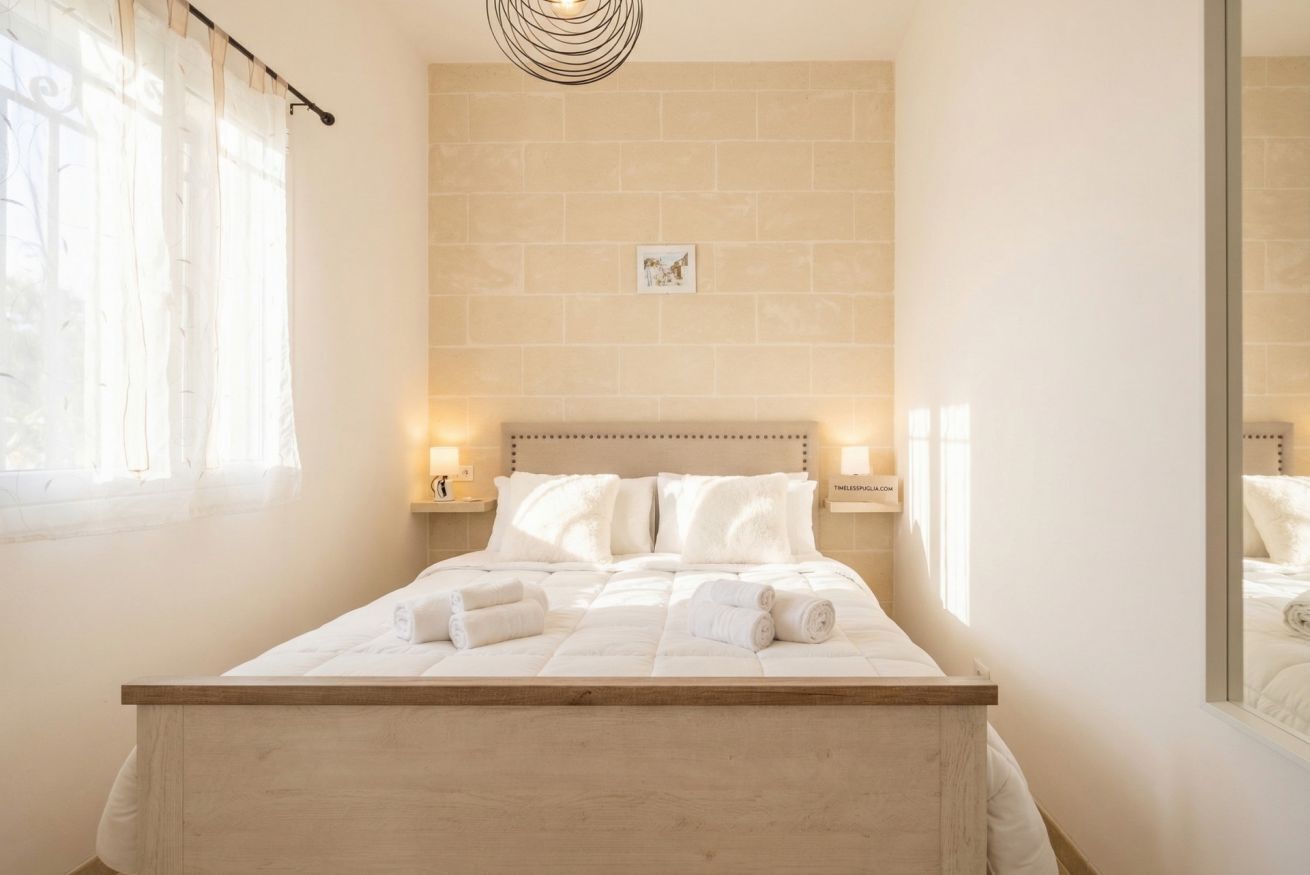 Un lit bien fait, avec du linge de lit blanc et des serviettes pliées, une tête de lit en bois clair et un tableau accroché au mur, ainsi que deux lampes de chevet posées sur des tables de nuit.