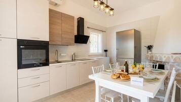 A modern kitchen with white cabinetry, a built-in oven, a stainless steel range hood, and a dining area with a white table set for two.