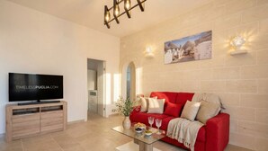 Ein modernes Wohnzimmer mit einem roten Sofa, einem Glastisch, einem Fernseher auf einem Holzboden und einem Gemälde an der Wand.
