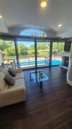 A spacious living room with a large window, a sofa, a coffee table, and a fireplace. - Picturesque Luxury Waterside Villa for Max. 6 Guests group (Niagara Falls)