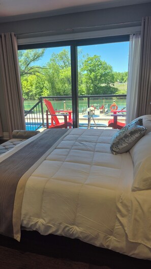 A hotel room with a large bed, a view of a lake, outdoor seating, and a railing. - Picturesque Luxury Waterside Villa for Max. 6 Guests group (Niagara Falls)