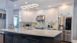 Een moderne keuken met een groot eiland, barkrukken, roestvrijstalen apparatuur en hanglampen.