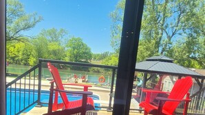 Uitzicht vanuit een kamer met een groot raam op een zwembadgedeelte met rode stoelen en een gazebo.