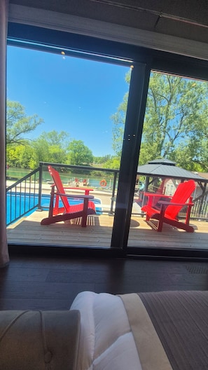 A view from a room with a large window overlooking a pool area with red chairs and a gazebo.