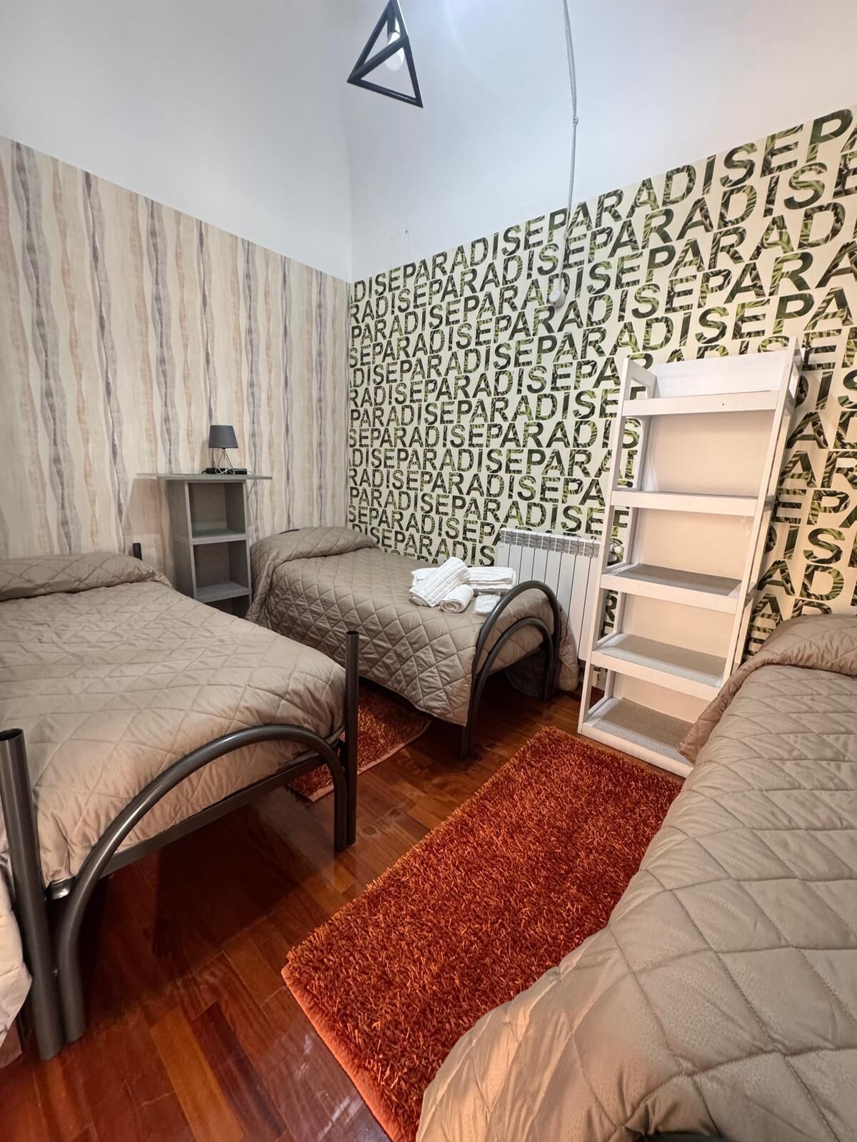 A bedroom with two beds, a nightstand, a shelf unit, and a patterned wall.