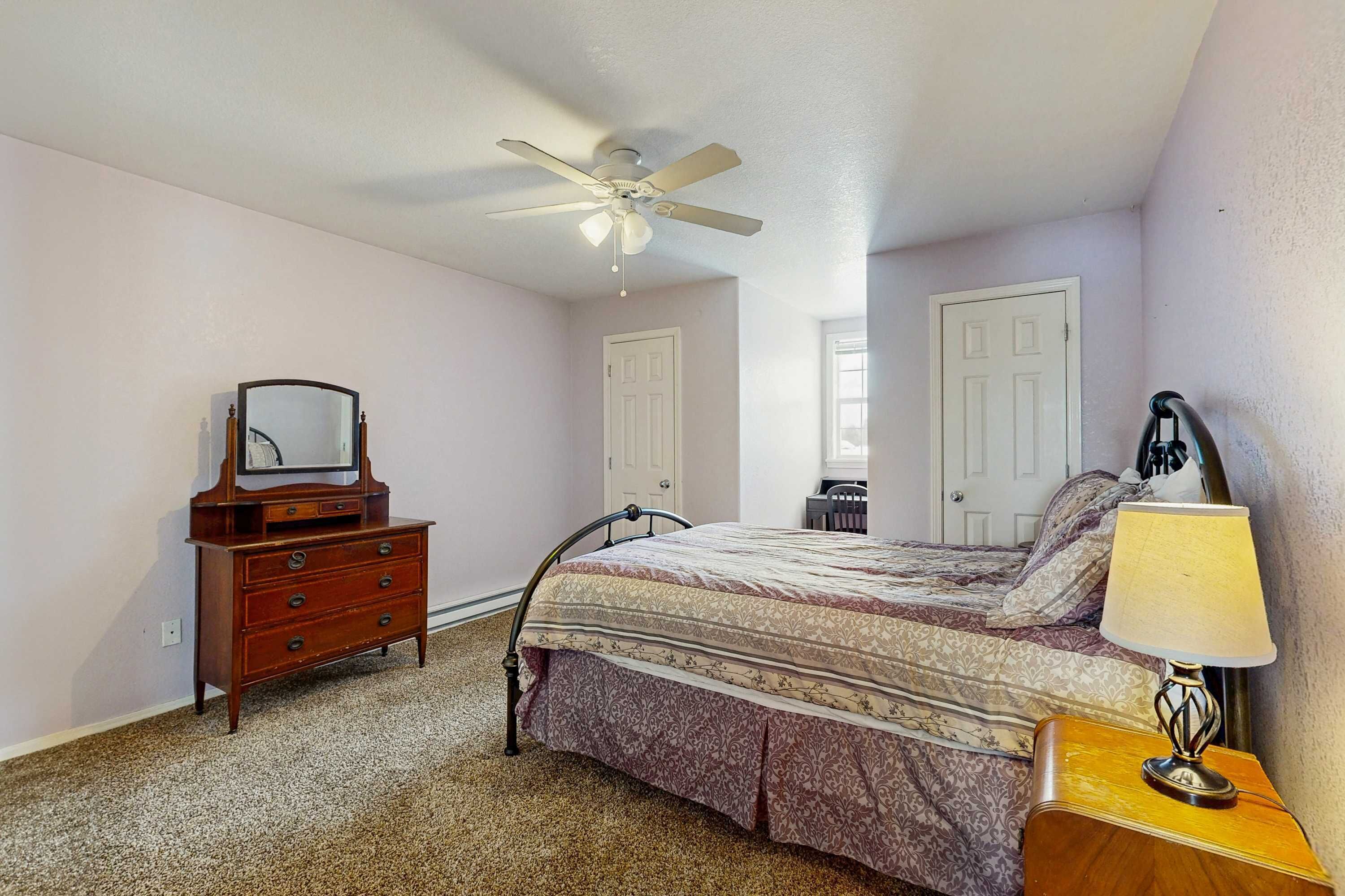 A bedroom with a bed, dresser, mirror, ceiling fan, and bedside lamp.