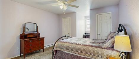 A bedroom with a bed, dresser, mirror, ceiling fan, and bedside lamp.