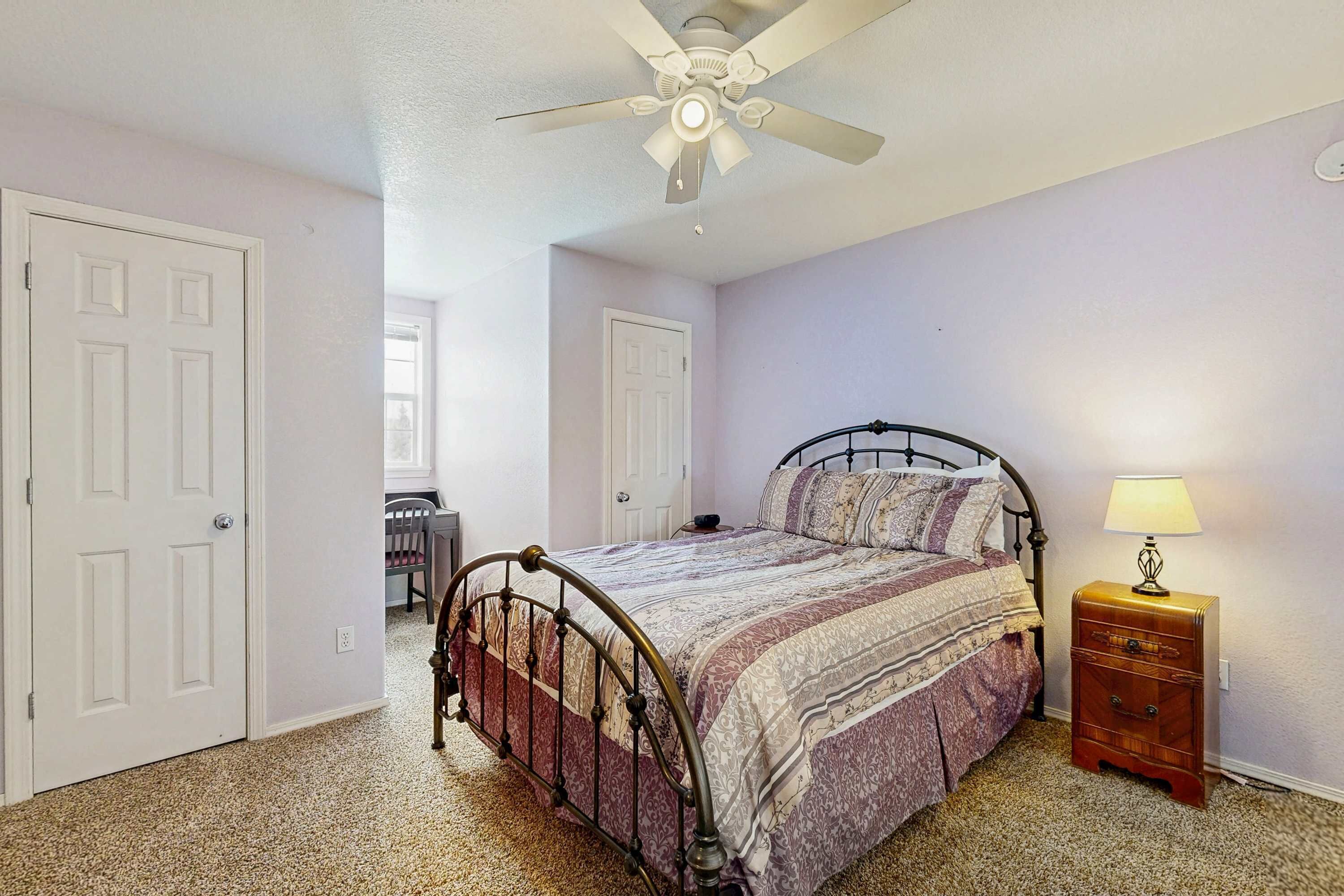 Une chambre à coucher avec un lit, une table de chevet, un ventilateur de plafond et une porte.