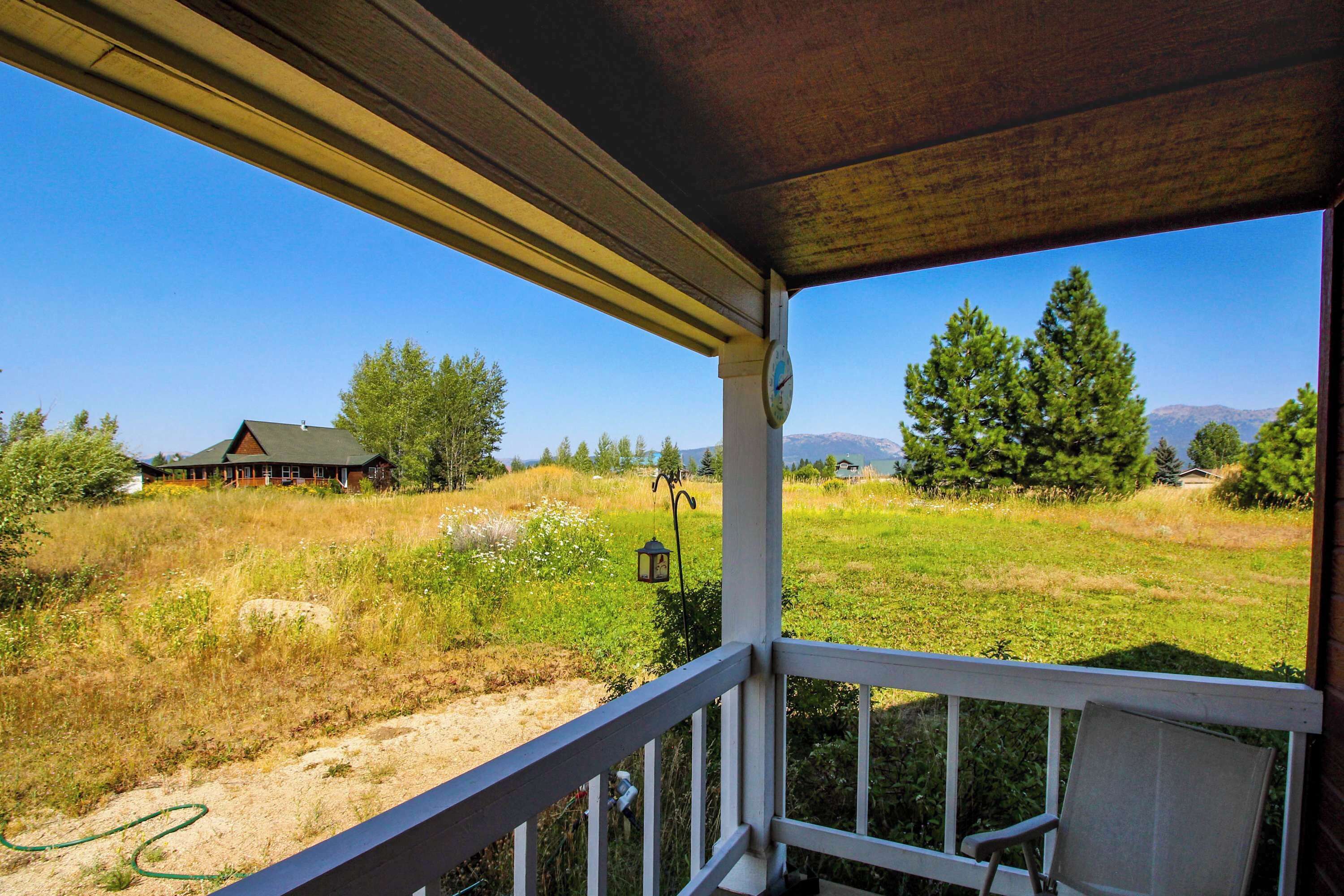 Varanda com vista para um campo gramado, uma casa e árvores.