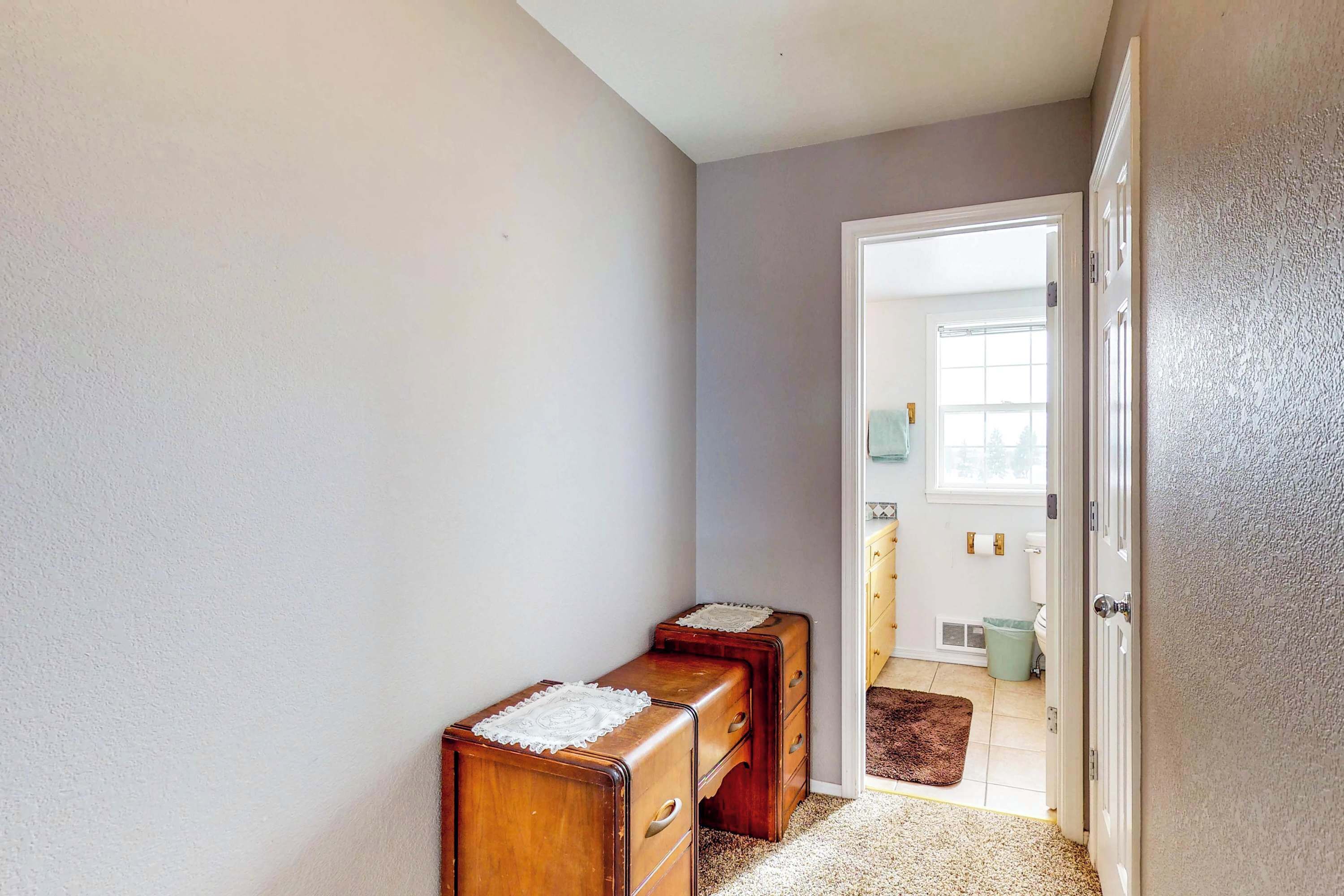 A hallway with two wooden dressers, a door leading to a bathroom, and a carpeted floor.