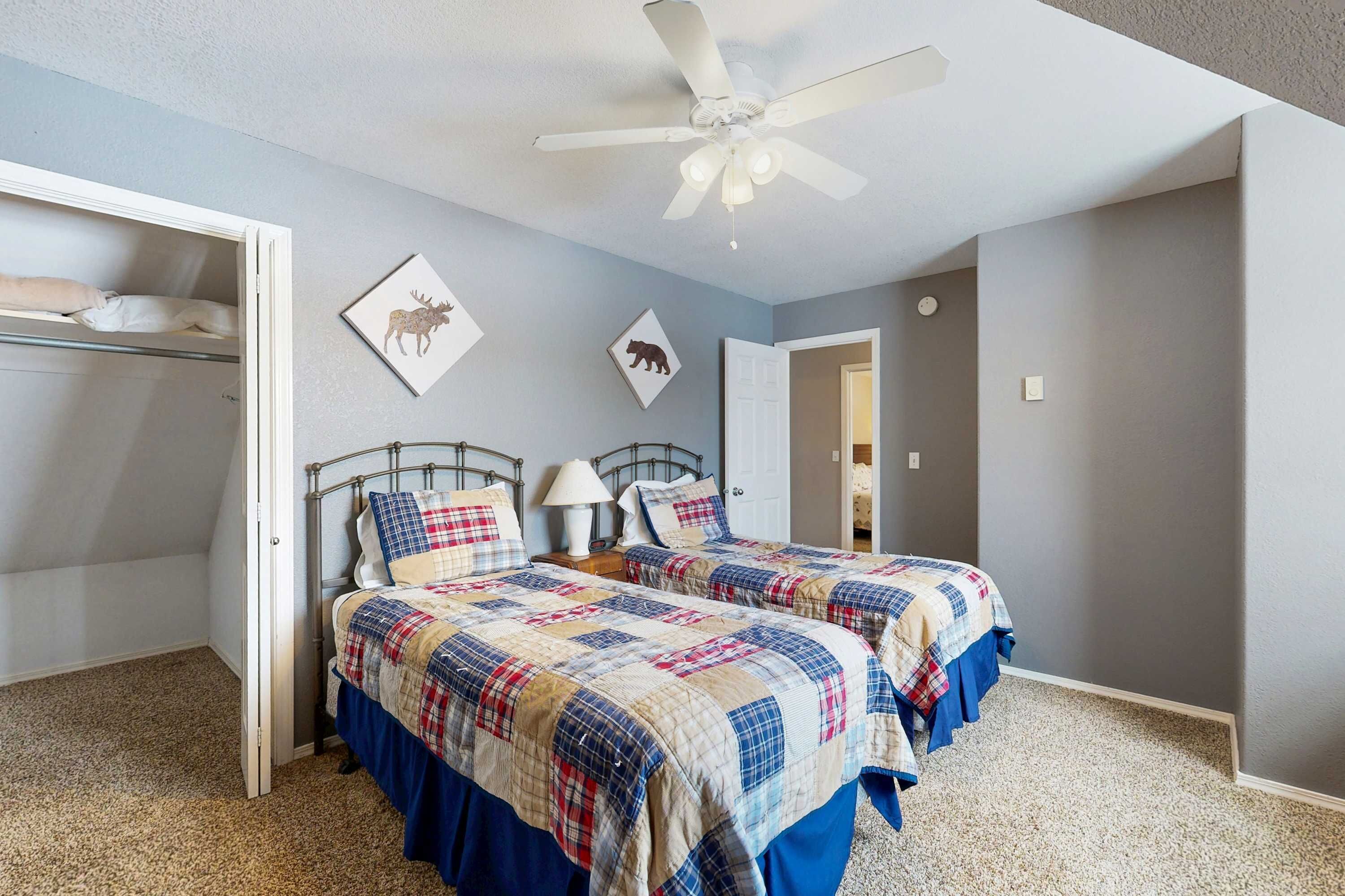 A bedroom with two beds, a ceiling fan, and a wardrobe.