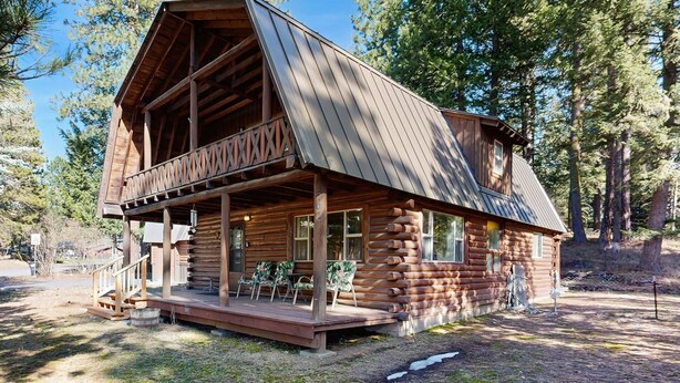 Een vakantiehuisje van hout met een balkon, een houten terras en een veranda met stoelen.