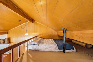 A wooden cabin room with a bed, a wooden ceiling, and a hanging light fixture.