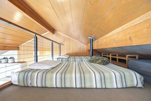 Habitació amb sostre de fusta, un llit amb roba de llit a ratlles, una finestra i una taula petita amb contenidors.