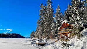 Uma cabana com fachada de madeira, cercada por árvores cobertas de neve e um céu azul límpido.