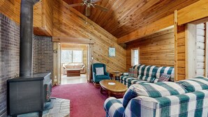 L'intérieur d'une cabane en rondins, avec une cheminée, un ensemble de canapés, un plafond en bois et une vue à travers une porte.