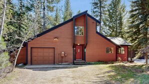 Une cabane en bois à deux étages, avec un garage, une porte d’entrée rouge et un petit porche.