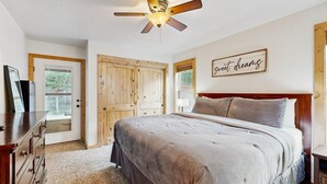 Ein Schlafzimmer mit Bett, Holzschrank, Deckenventilator und einem motivierenden Spruch an der Wand.