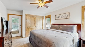 A bedroom with a bed, wooden wardrobe, ceiling fan, and a motivational quote on the wall.
