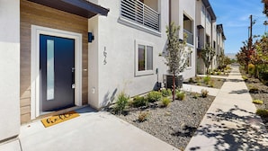 A modern building with a grey facade, a blue door, and a small garden area with plants and a gravel path. - Modern Townhouse, Centrally Located Near BSU (Boise)