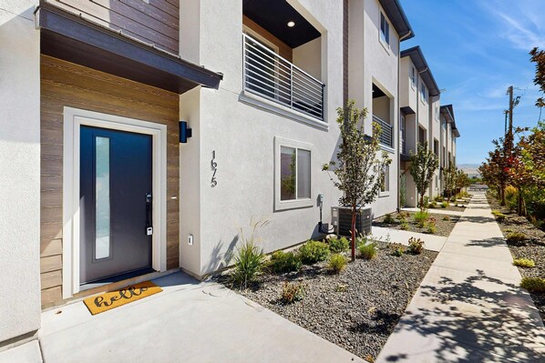 A modern building with a grey facade, a blue door, and a small garden area with plants and a gravel path. - Modern Townhouse, Centrally Located Near BSU (Boise)