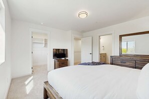 A bedroom with a large bed, a TV on a wooden stand, a dresser, and a mirror above the dresser. - Modern Townhouse, Centrally Located Near BSU (Boise)