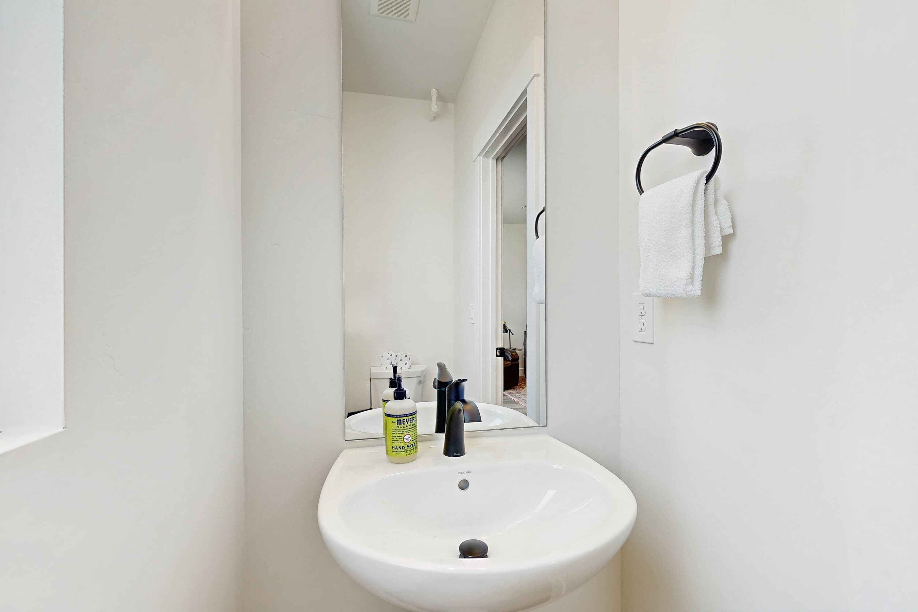 Un baño con lavamanos blanco, un espejo y un perchero para toallas.