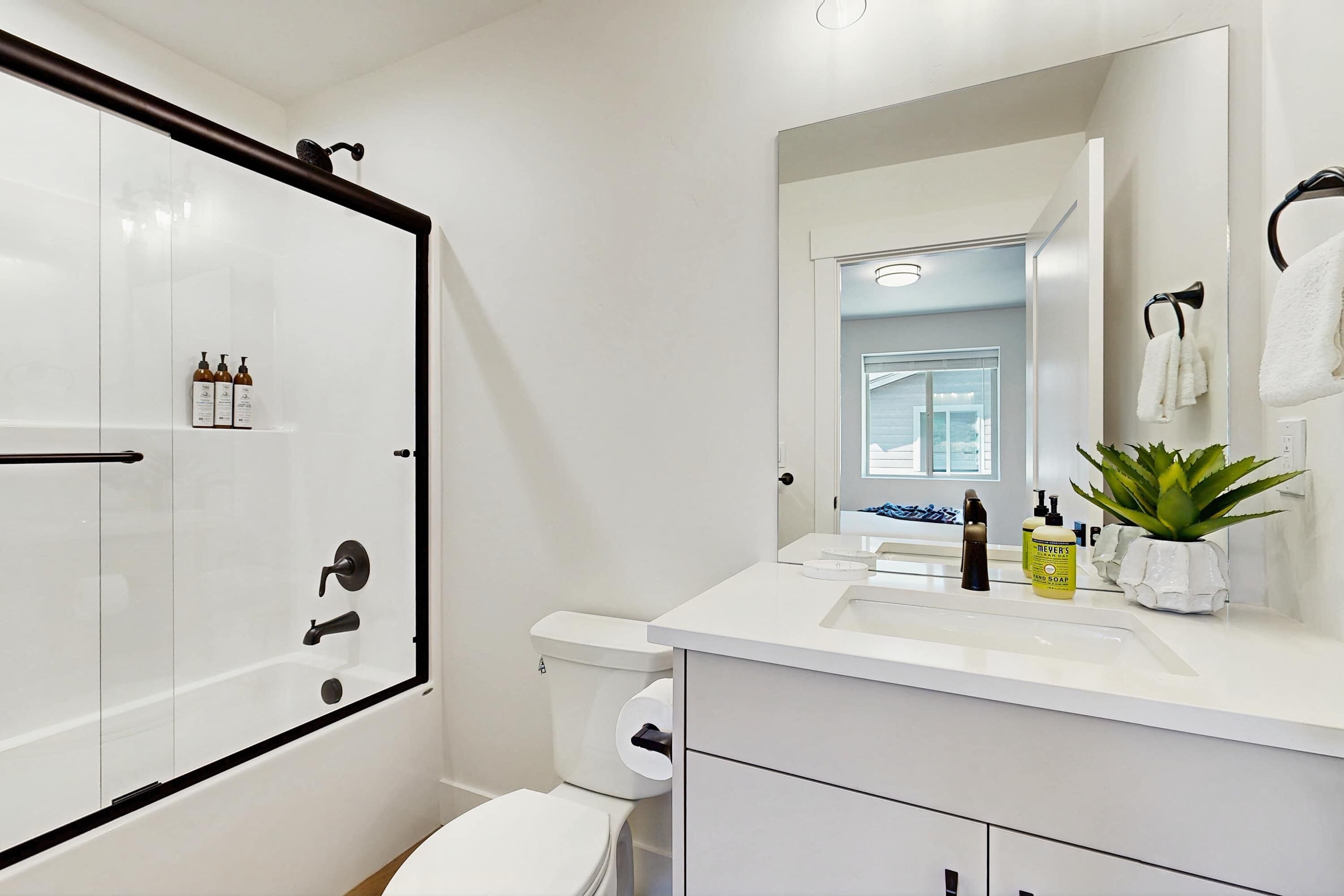 Ein modernes Badezimmer mit einer einteiligen Duschkabine, Toilette, Waschbecken und Badutensilien sowie einem Spiegel.