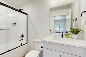 A modern bathroom with a glass-enclosed shower, a toilet, a sink with toiletries, and a mirror. - Modern Townhouse, Centrally Located Near BSU (Boise)