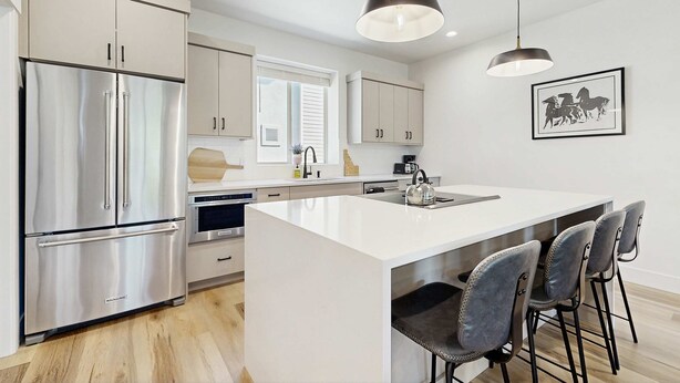 A modern kitchen with stainless steel appliances, a central island with bar stools, and pendant lighting. - Modern Townhouse, Centrally Located Near BSU (Boise)