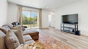 A modern living room with a large sofa, a flat-screen TV on a stand, and a large window with curtains. - Modern Townhouse, Centrally Located Near BSU (Boise)