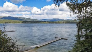 Un lac paisible avec une jetée qui s’avance sur l’eau, entouré d’arbres et bordé de montagnes en arrière-plan.