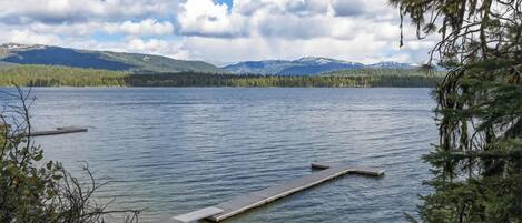A calm lake with a dock extending into the water, surrounded by trees and mountains in the background.