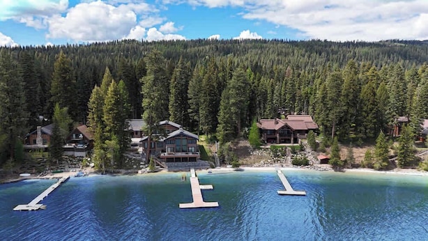 Un chalet au bord du lac, doté de plusieurs cabanes, d’un quai et entouré d’une forêt.
