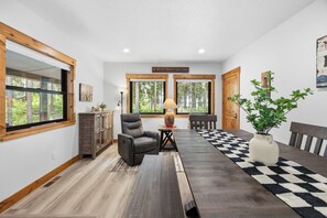 A room with a large wooden dining table, a leather chair, a small side table with a lamp, and a potted plant.