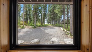 Une vue à travers une fenêtre sur une zone boisée, avec un sentier de gravier et des structures en bois.
