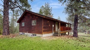 A wooden cabin with a porch, surrounded by trees.