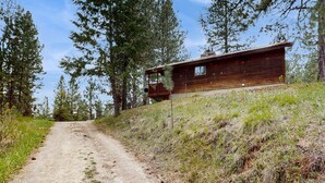 A wooden cabin with a porch, surrounded by trees and a dirt path. - Cascade Cabin | Deck, 2 Living Rooms + Fireplaces (Cascade)