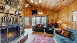 A cozy cabin interior with a stone fireplace, wooden walls, a leather sofa, and a ceiling fan. - Cascade Cabin | Deck, 2 Living Rooms + Fireplaces (Cascade)