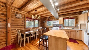 A log cabin interior with a dining area, kitchen, and a large window.