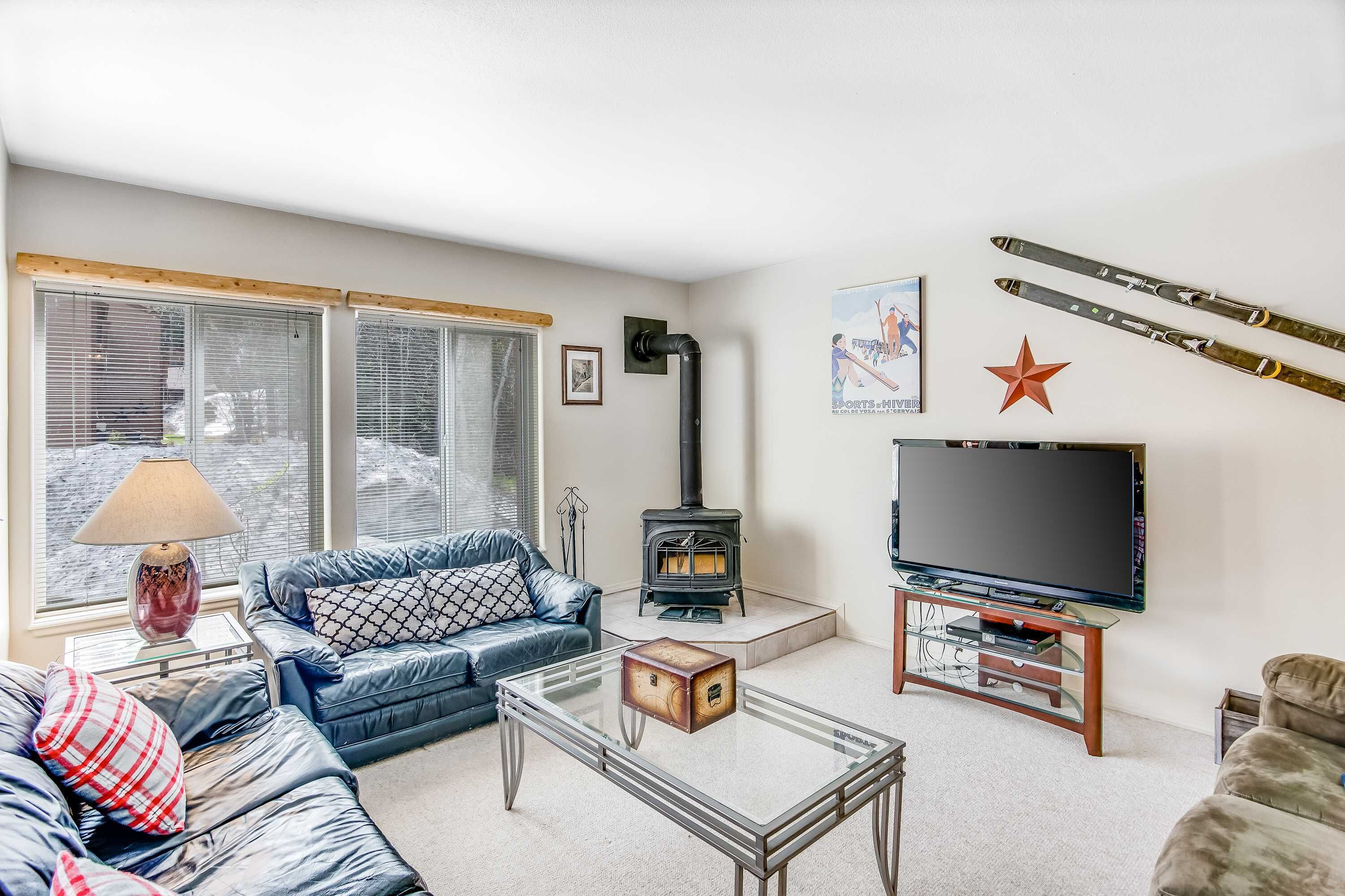 A living room with a sofa, a coffee table, a TV, a fireplace, and skis on the wall.