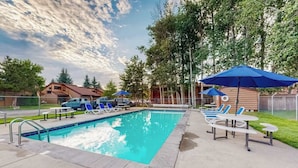 Ein Swimmingpool mit Liegestühlen und Sonnenschirmen, umgeben von Bäumen und einem Zaun.