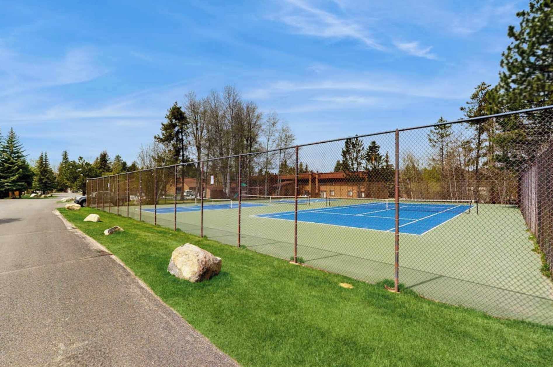 Una cancha de tenis rodeada por una cerca de malla metálica, con una carretera pavimentada contigua.