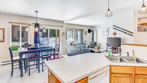 Eine moderne Küche mit Kochinsel, ein Essbereich mit Tisch und Stühlen sowie ein Wohnbereich mit Sofa und Fernseher.
