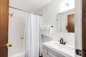 Un baño con ducha, lavamanos y espejo.