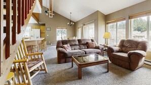 Ein Wohnzimmer mit einem braunen Ledersofa, einem Glastisch, Holzschaukelstühlen und einer Küche im Hintergrund.