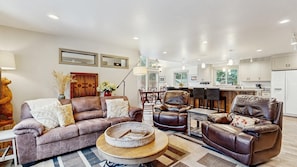 A modern living room with a sofa, two armchairs, a coffee table, and a dining area with a table and chairs.